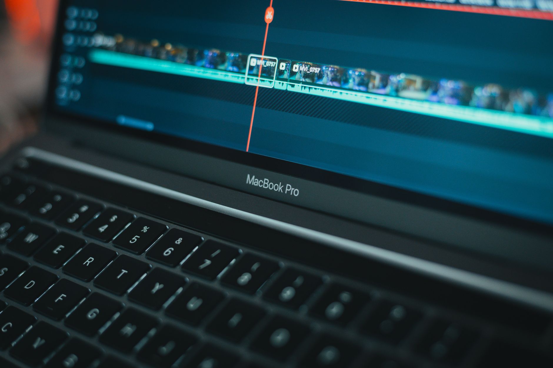 Gros plan d’un ordinateur portable affichant une timeline de montage vidéo avec des clips et une piste audio, clavier au premier plan.